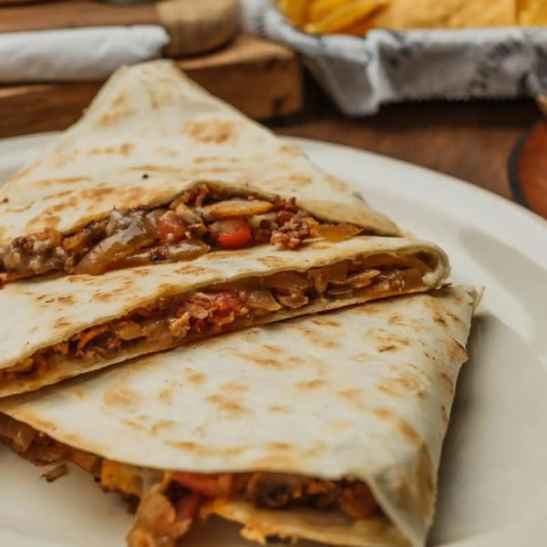 Two quesadilla halves filled with meat, cheese, onions, and peppers on a white plate.