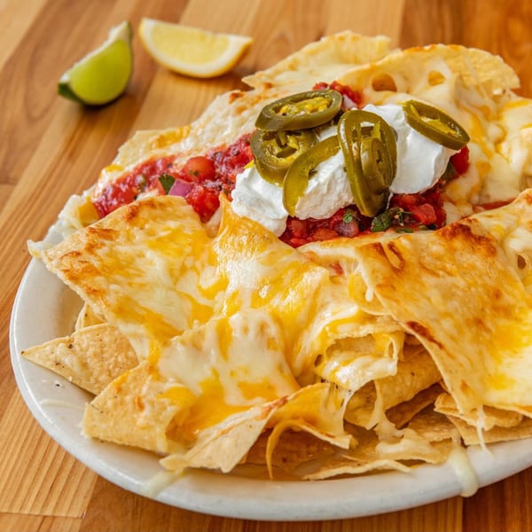 Cheesy nachos topped with salsa, sour cream, and jalapeños, with lime and lemon wedges nearby.