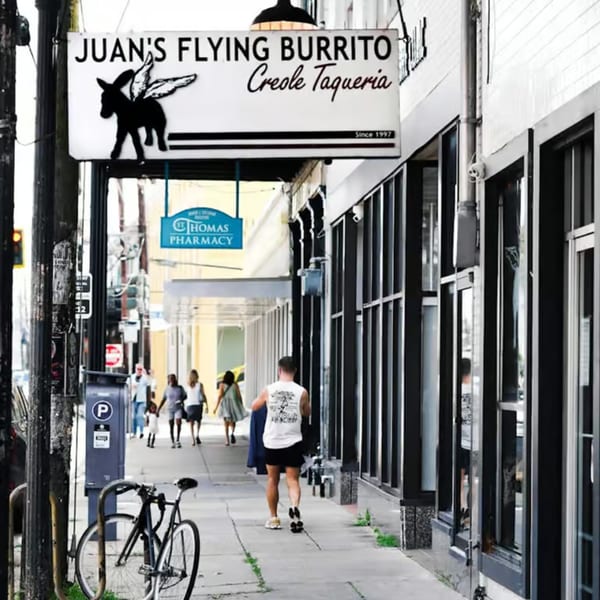 A street view of Juan's Flying Burrito Creole Taqueria sign, with people walking on the sidewalk.