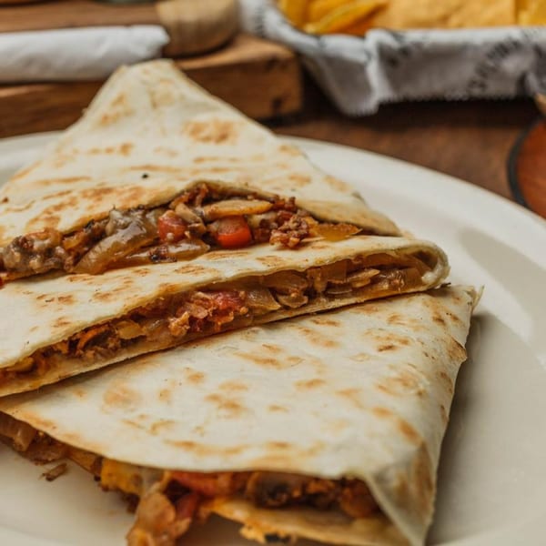 Two quesadilla halves filled with meat, cheese, onions, and peppers on a white plate.