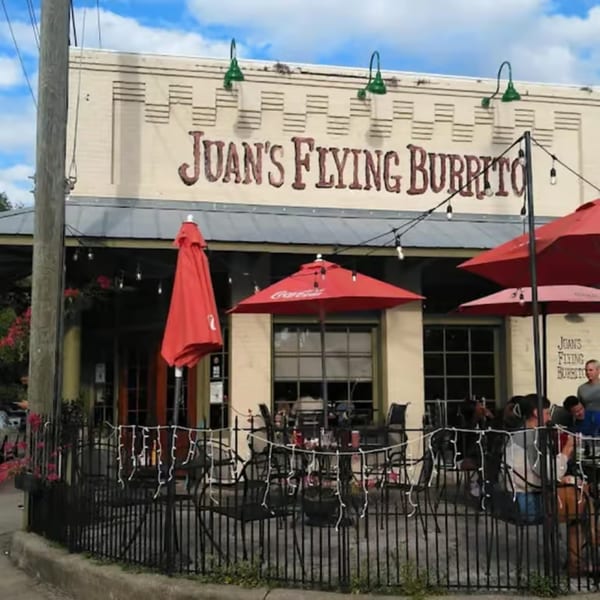 Exterior of Juan's Flying Burrito with outdoor seating, red umbrellas, and string lights.