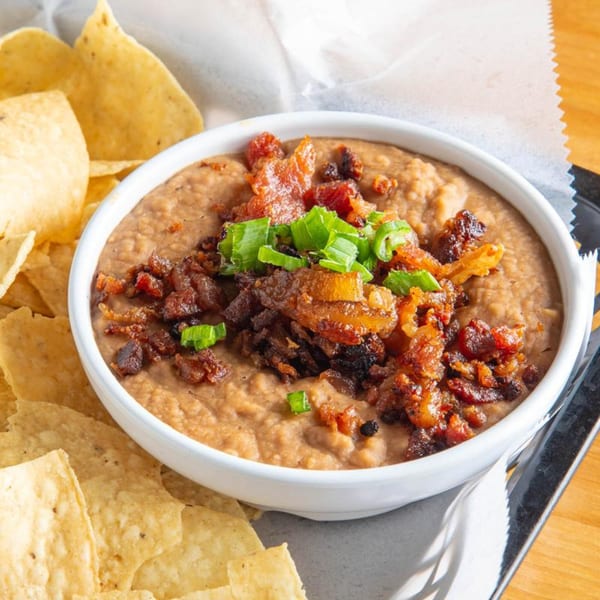 Refried beans topped with crispy bacon bits and green onions, served with tortilla chips.