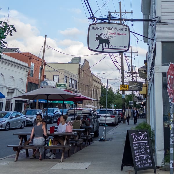 Juan's Flying Burrito sign above a street scene with people dining outdoors at picnic tables.