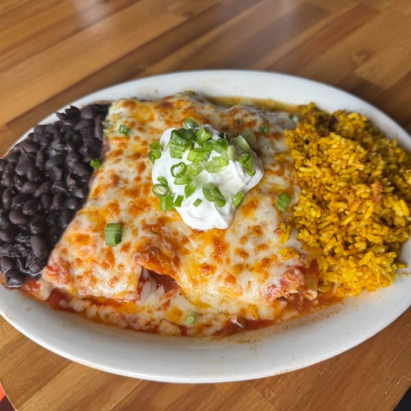 Cheesy enchiladas topped with sour cream and green onions, served with black beans and yellow rice.