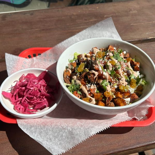 A sweet potato bowl with raisins, seeds, and sauce, next to a small bowl of pickled red cabbage.