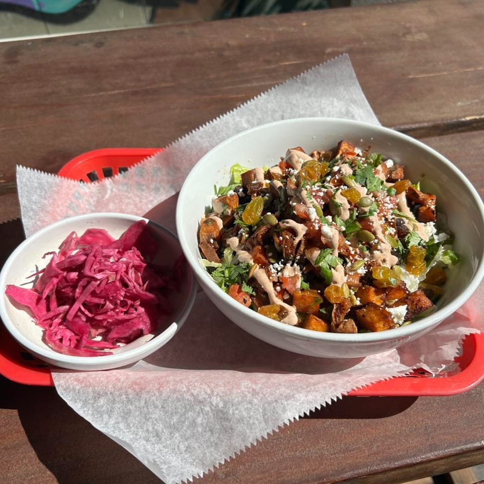A sweet potato bowl with raisins, seeds, and sauce, next to a small bowl of pickled red cabbage.