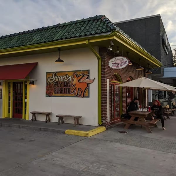 Juan's Flying Burrito restaurant exterior with a green roof, outdoor seating, and two patrons.