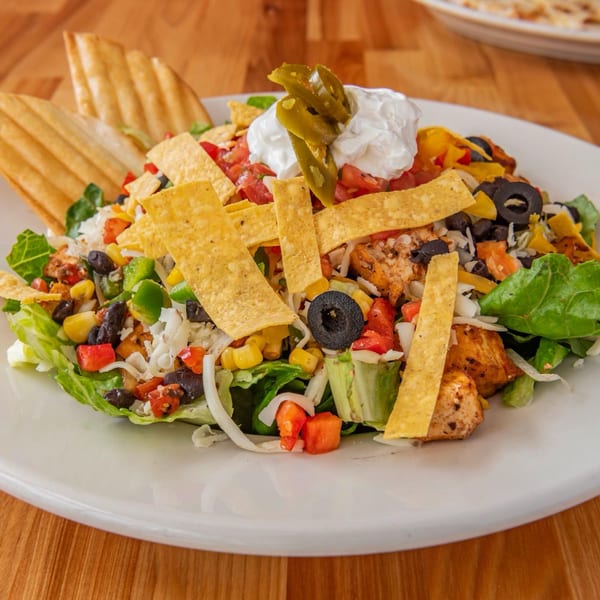 A vibrant taco salad with grilled chicken, fresh vegetables, tortilla strips, sour cream, and jalapeños.