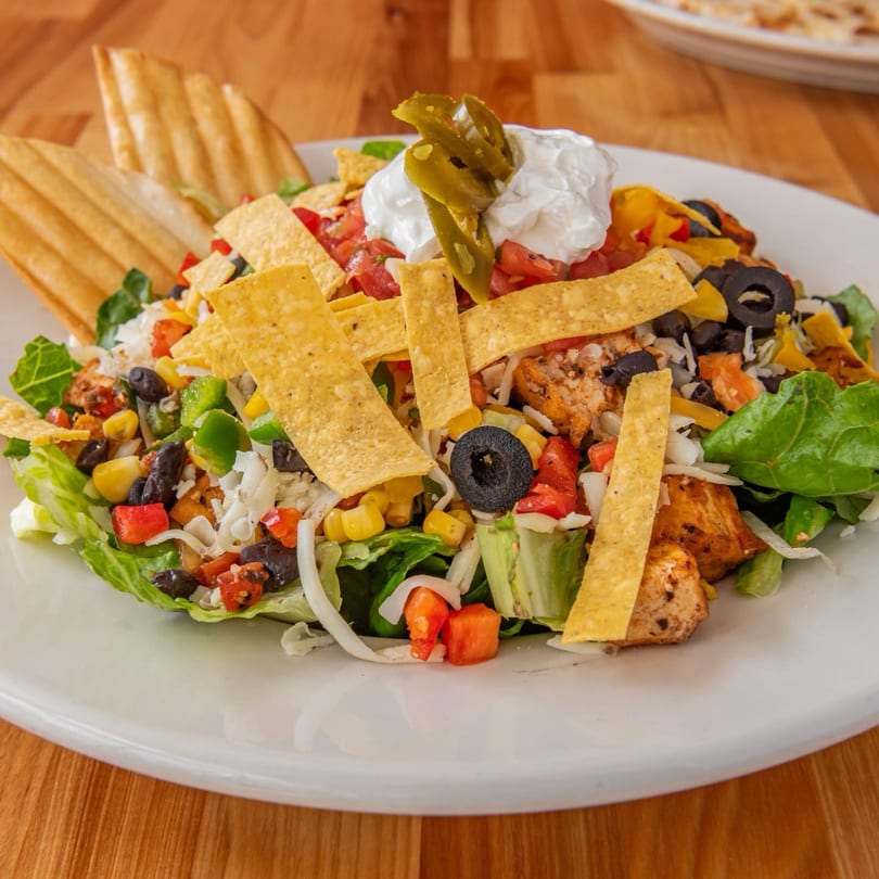 A vibrant taco salad with grilled chicken, fresh vegetables, tortilla strips, sour cream, and jalapeños.