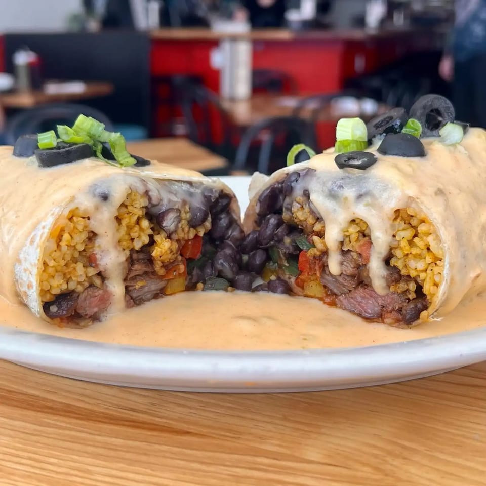A large burrito, cut in half, revealing steak, rice, black beans, and peppers, covered in cheese sauce.