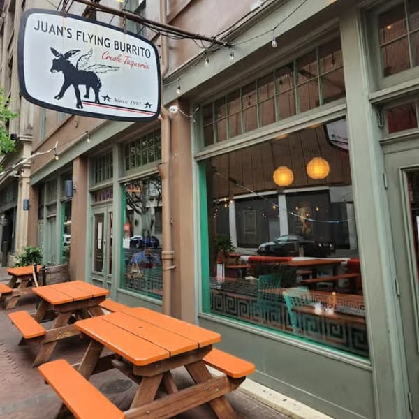 Exterior of Juan's Flying Burrito, a Creole Taqueria, with orange picnic tables and large windows.