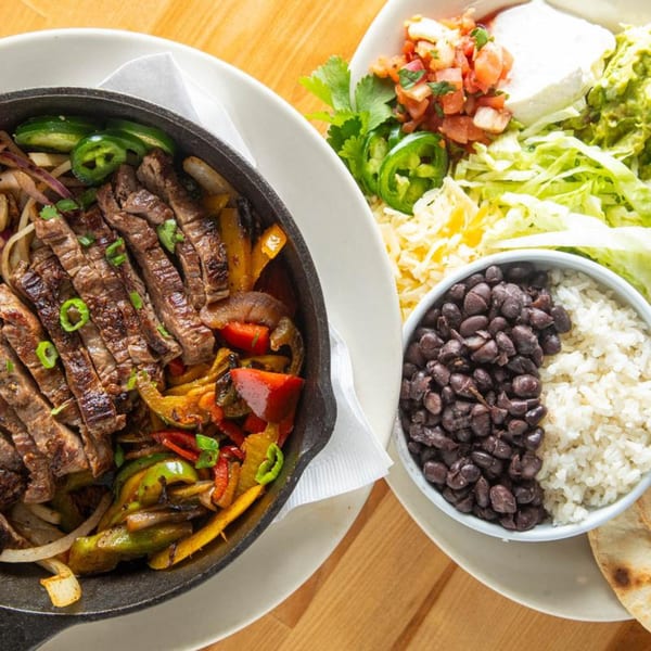 Sizzling steak fajitas with peppers and onions, served with rice, black beans, and fresh toppings.